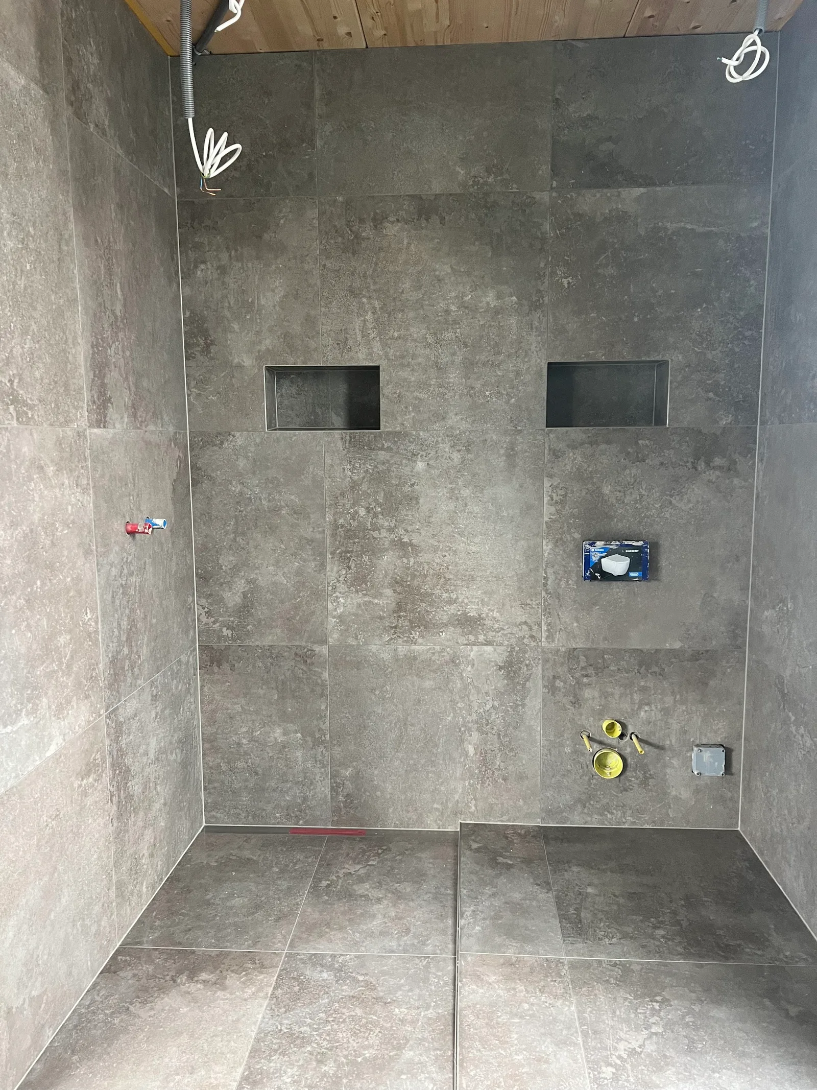 Begehbare Dusche mit großformatigen grauen Fliesen an Wand und Boden und zwei Wandnischen, noch ohne Armaturen
