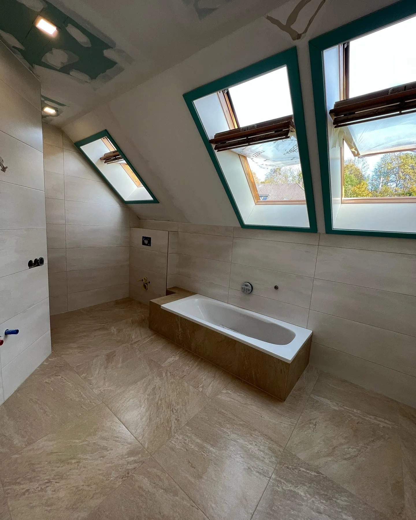 Bad unter der Dachschräge mit drei Dachfenstern, Badewanne mit Holzverkleidung und beigen Bodenfliesen